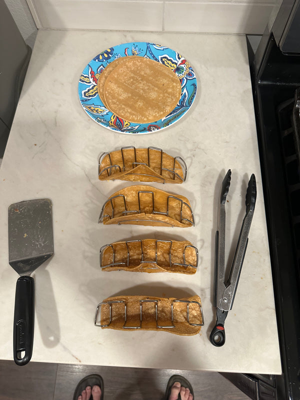 Baked taco shells on a marble surface with tongs and a spatula.
