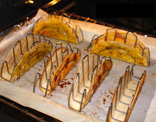 Tortillas folded around stainless steel taco shaper in the oven baking to a crisp